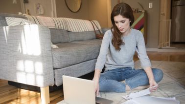 woman sitting on floor with open laptop paying student loans 