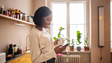 Woman in a kitchen drinking coffee and reading a story on her phone about what makes up a good financial plan