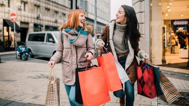 Two women carrying shopping bags trying to prevent holiday overspending.  
